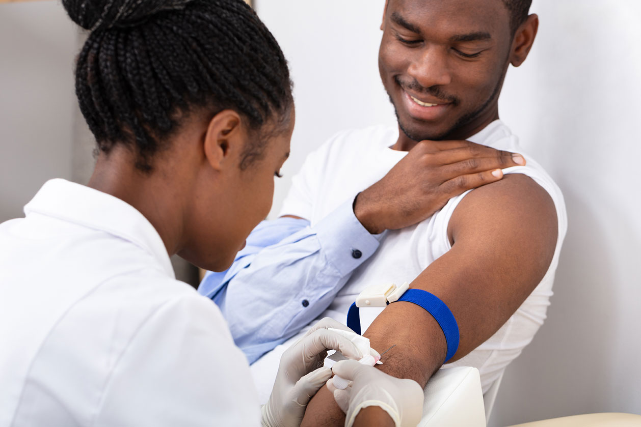 A nurse takes blood from the arm of a young African American man